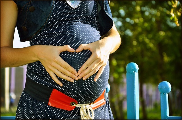Kobieta w ciąży trzyma na brzuchu ręce ułożone w serce