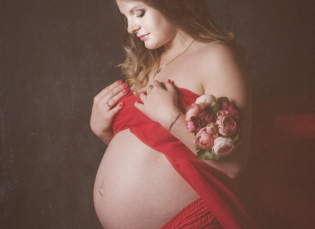 Kobieta w ciąży trzyma na ręce rozwinięte róże