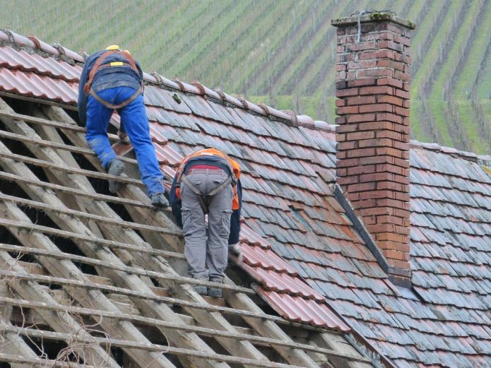 Dekarze układający dachówkę na drewnianej konstrukcji dachu domu jednorodzinnego.
