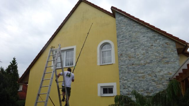 Fachowiec na drabinie maluje ścianę budynku